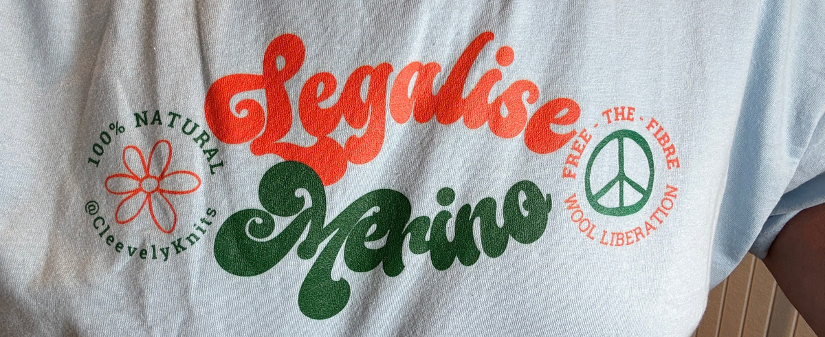 A person wearing a light blue t-shirt with a colorful graphic print that reads 'Legalise Marino' in orange and green script, with a peace sign and flower design.